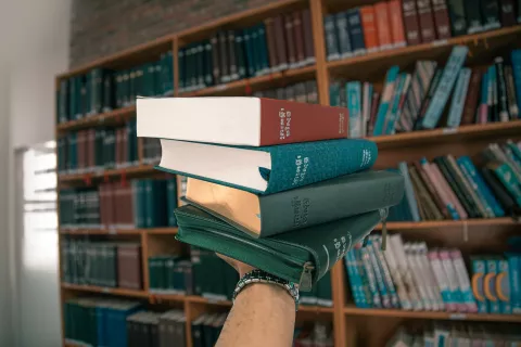 Mano che sorregge libri con libreria sullo sfondo