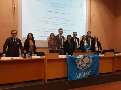 Persone al tavolo del convegno con diapositiva proiettata e bandiera di Unicef