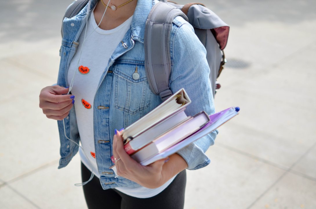 Foto di una ragazza con lo zaino che regge in mano dei libri