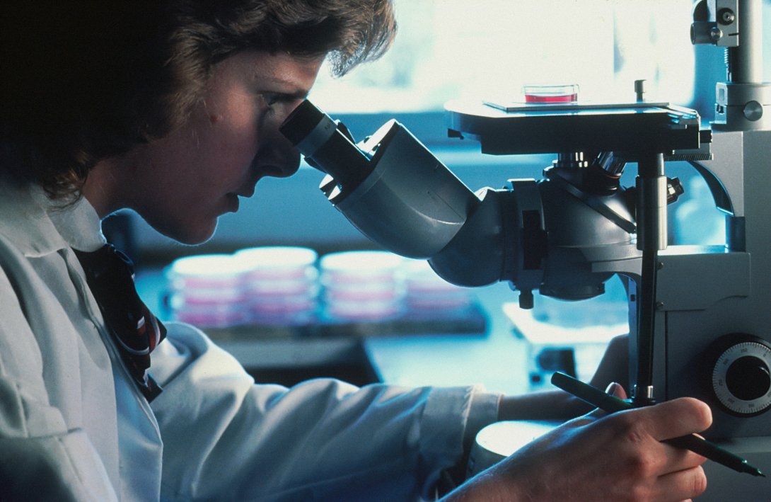 Foto di un uomo con un camice da laboratorio che usa un microscopio