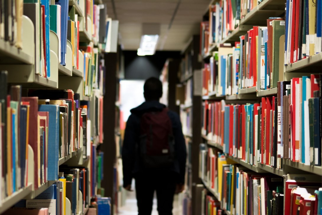 Persona che cammina tra due scaffali di libri