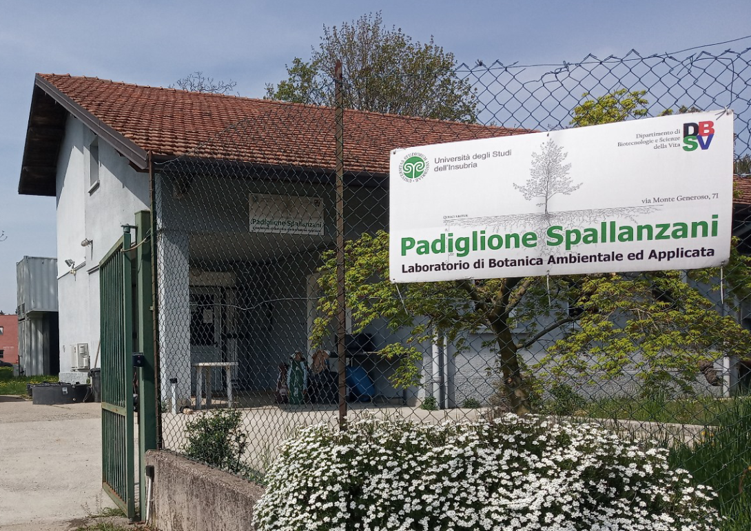 Ingresso all'edificio, con recinzione e cespuglio fiorito, oltre a cartello con scritta "Padiglione Spallanzani"